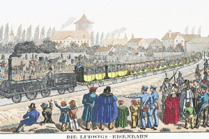Eine Gruppe von Menschen, die um und in einem Zug auf einem Gleis stehen, mit Gebäuden und Bäumen im Hintergrund und einem Text unten, der "Ludwigs-Eisenbahn, die erste Bahnstation in Deutschland" liest.