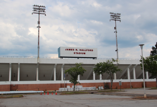 Großes Stadion namens James R. Hallford Stadium in Houston, Texas, mit einem Namen auf der Wand, umgeben von Bäumen, Pfählen, Lichtern und Verkehrskegeln unter einem bewölkten Himmel.