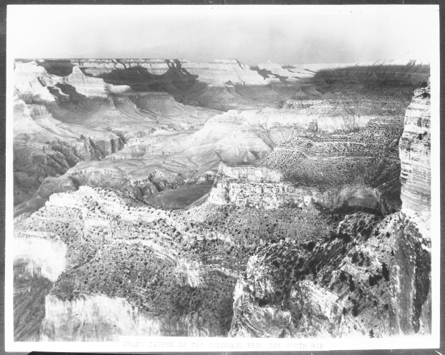 Schwarzes und weißes Foto des Grand Canyon mit geschichteten Felsformationen und weitem Himmel, mit Text unten.