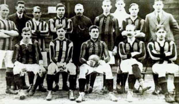 Ein Schwarz-Weiß-Foto einer Fußballmannschaft, bei der einige stehen und einige sitzen, vor einer Wand, mit dem Text "Ballymena Football Club" unten.