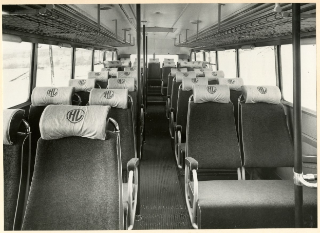 Altes Schwarz-Weiß-Foto eines Busses mit mehreren Sitzreihen, senkrechten Stangen und Glasfenstern, mit Text am unteren Rand.