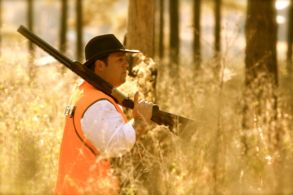 Eine Person mit einer Waffe steht vor Pflanzen mit Bäumen im Hintergrund.