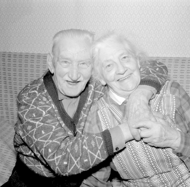 Schwarz-weiß-Foto eines älteren Paares, das sich auf einem Sofa umarmt und lächelt.