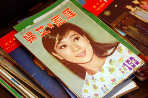 Eine Sammlung von Zeitschriften auf einem Tisch mit der vordersten Zeitschrift, die ein Bild einer Frau zeigt.