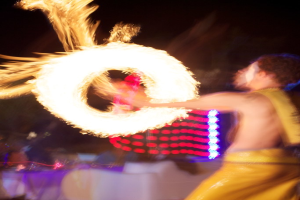 Mann spielt mit dem Feuer, mit Lichtern im Hintergrund.