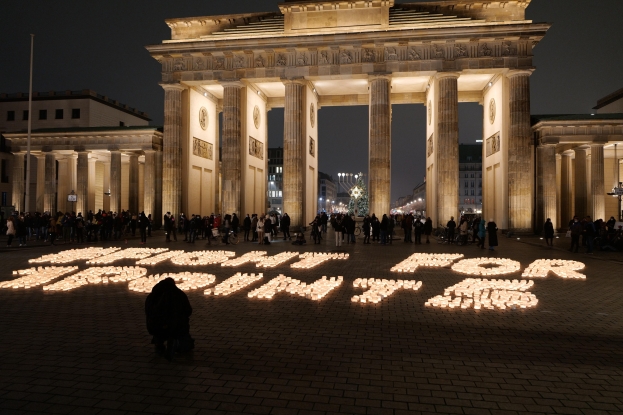 Eine Gruppe von Menschen steht vor dem beleuchteten Brandenburger Tor in Berlin, Deutschland, umgeben von Gebäuden, Pfählen und Lichtern, und die Wörter 'Kampf für die Freiheit' sind auf dem Boden im Vordergrund geschrieben.