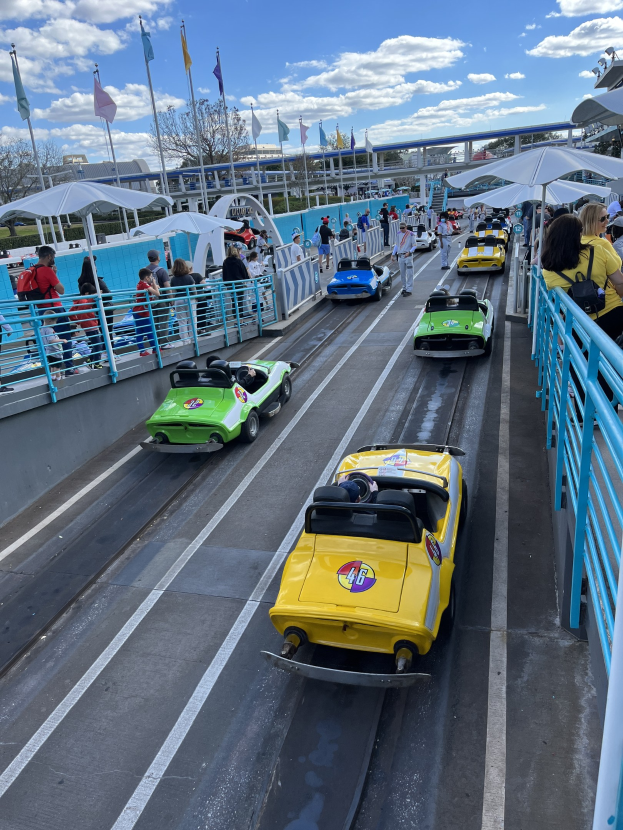 Menschen auf einer Achterbahn in Disney's Hollywood Studios, mit Geländern, Fahnen, Bäumen, Gebäuden und einem bewölktem Himmel im Hintergrund.