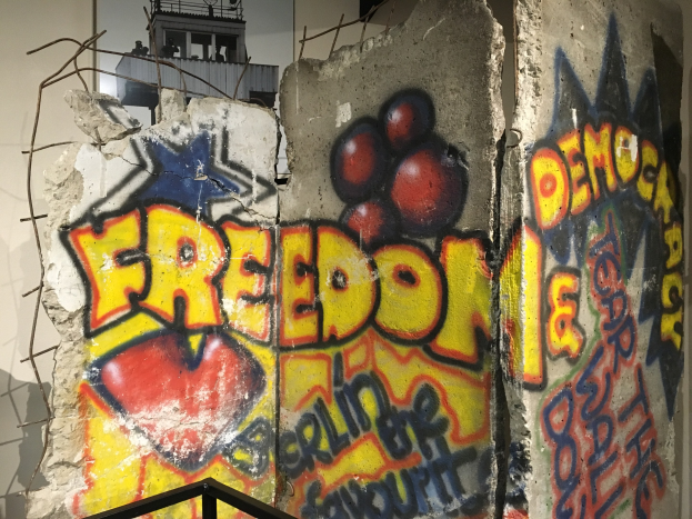 Eine Wand mit Graffiti, das in fetten schwarzen Buchstaben "Freiheit und Demokratie" lautet, ein Geländer unten und ein Gebäude mit Fenstern im Hintergrund.