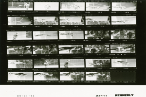 Schwarzes und weißes Foto eines Mannes in einem weißen Hemd und Shorts, der Tennis spielt und einen konzentrierten Gesichtsausdruck hat, vor einem Filmstreifen-Hintergrund.