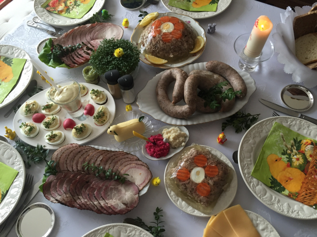 Ein langer Tisch mit verschiedenen Gerichten, Besteck, Gläsern und Kerzen, umgeben von Stühlen, was auf ein traditionelles deutsches Osteressen hinweist.