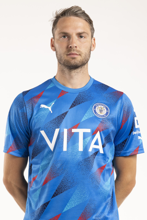 Ein Mann steht vor einem weißen Hintergrund und trägt ein blaues Leicester City Away-Shirt aus der Saison 2018-19, auf dem sich das Team-Logo und Text auf der Vorderseite befinden.