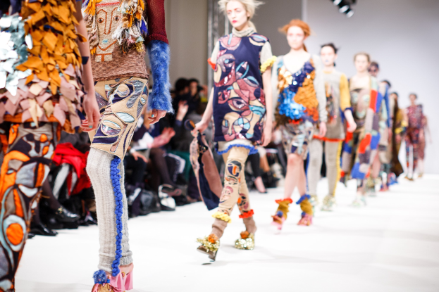 Eine Gruppe Von Frauen Läuft Den Laufsteg Bei Der London Fashion Week entlang, Mit Sitzenden Zuschauern Und Heller Beleuchtung Im Hintergrund.