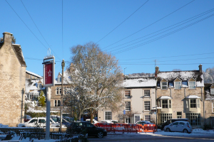 Fahrzeuge auf einer schneebedeckten Straße mit Häusern, Bäumen und Strommasten im Hintergrund, alles von Schnee bedeckt.