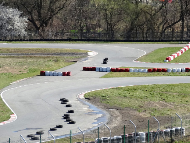 Rennstrecke mit zahlreichen Reifen, die entlang ihrer Ränder angeordnet sind und von Gras und Maschendrahtzaun umgeben ist, mit Bäumen im Hintergrund.