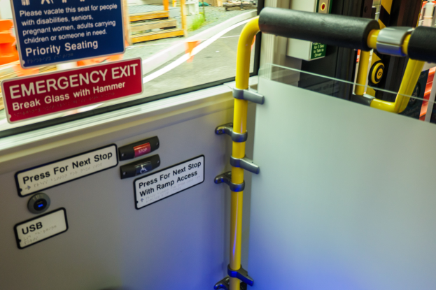 Notausgangsschild an einer Zugseite mit einer Tür, Griff und einem Glasfenster, das äußere Elemente wie eine Straße und Pfosten zeigt.