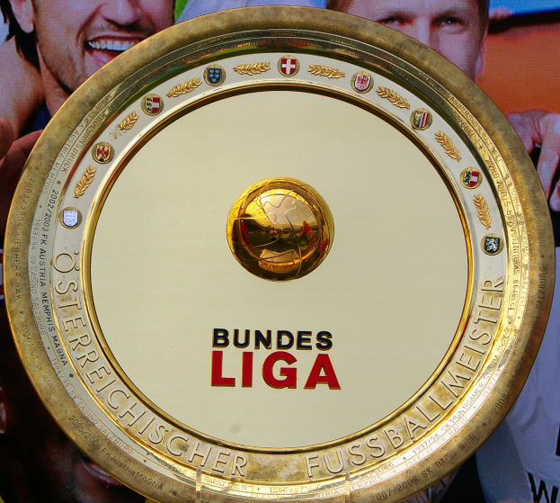 Goldener Schild mit "Bundesliga"-Text, gehalten von einem Mann, mit einem Banner im Hintergrund mit drei Personen.