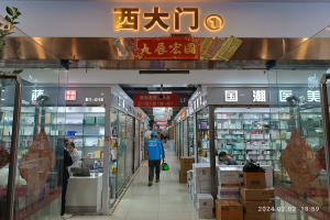 Innenansicht einer chinesischen Apotheke mit Glaswänden, einer Pflanze links, Regalen mit Artikeln, verstreuten Kartons und einer Namensschild oben.