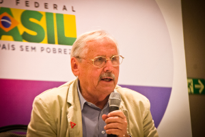 Eine Person, die in ein Mikrofon spricht und im Hintergrund ein Banner mit der Aufschrift 'Bundes' trägt.