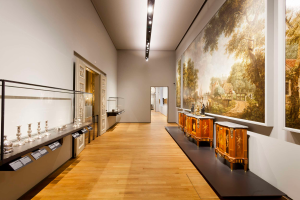 Ein Raum im Stedelijk Museum in Amsterdam, der verschiedene Kunstwerke, einschließlich Gemälde, Objekte, Texttafeln und eine Glasbox, zeigt.