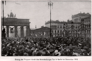 Große Menschenmenge vor dem Brandenburger Tor in Berlin, Deutschland, 1918, mit Menschen in Hüten und Fahnen, Säulen und Statuen des Tors im Hintergrund sowie Gebäuden und Laternenmasten.