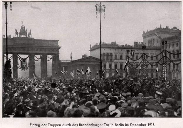 Große Menschenmenge vor dem Brandenburger Tor in Berlin, Deutschland, 1918, mit Menschen in Hüten und Fahnen, Säulen und Statuen des Tors im Hintergrund sowie Gebäuden und Laternenmasten.