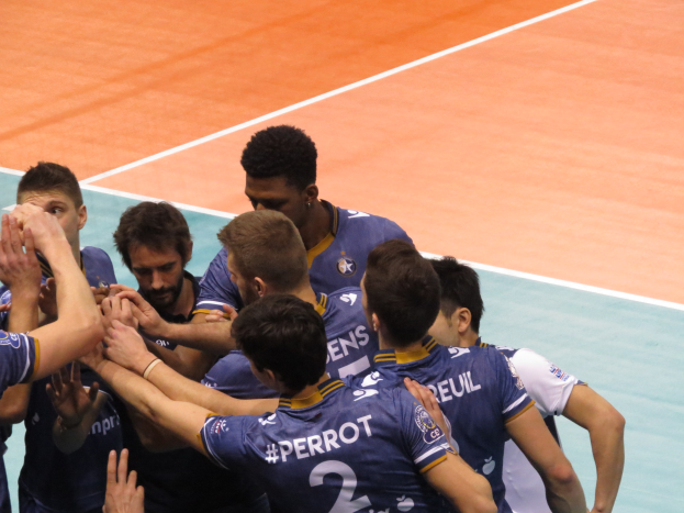 Gruppe von Männern in blauen "Ligue 1" T-Shirts feiert auf einem Volleyballfeld.