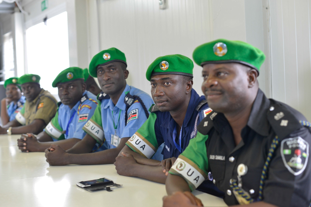 Gruppe von Polizeibeamten, die an einem Tisch sitzen, mit Mobiltelefonen und anderen Gegenst├Ąnden auf dem Tisch, in einem Raum mit Fenstern und Deckenleuchten.