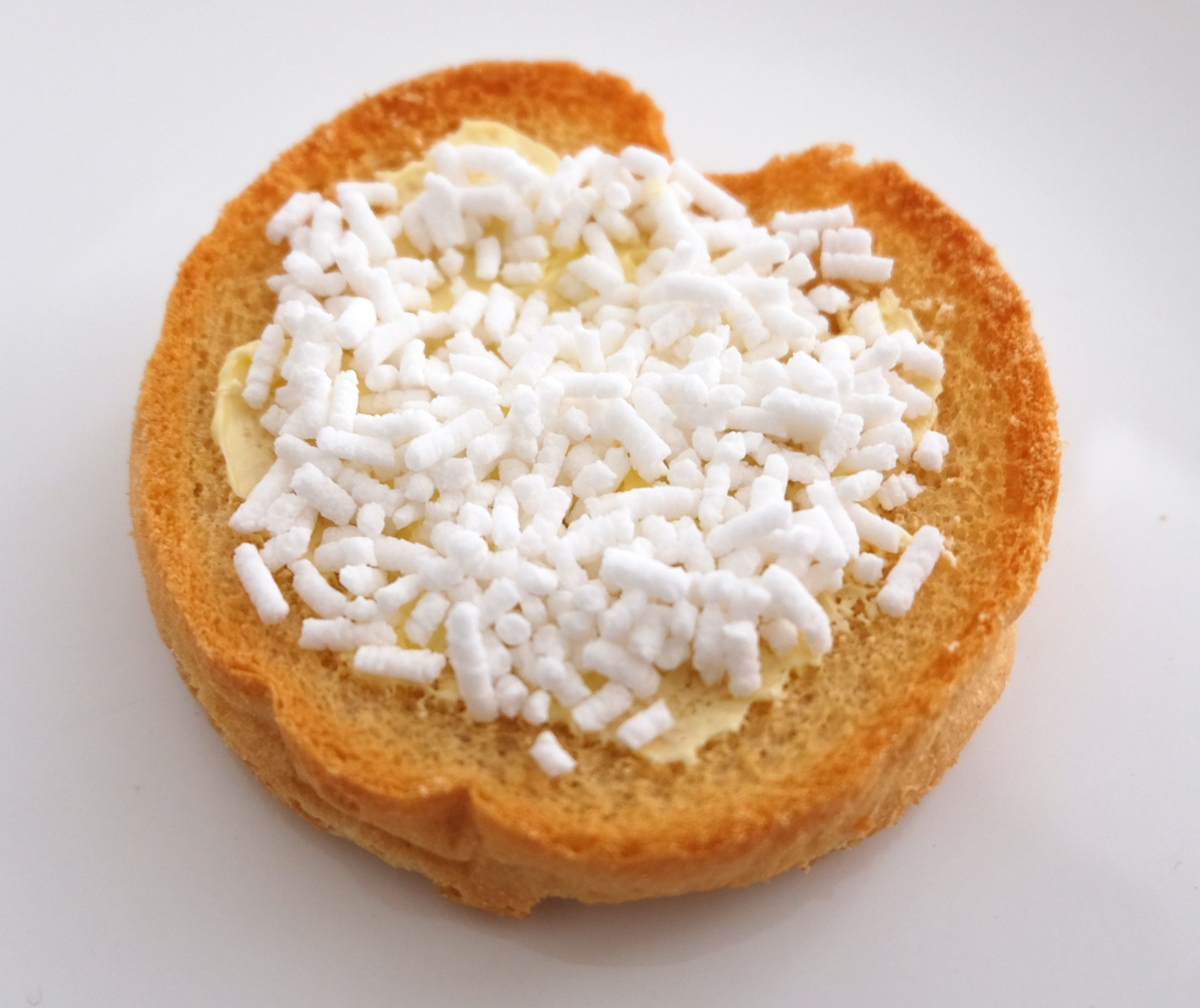 Herzförmiger Brotlaib mit Butter und weißem Zucker auf einer weißen Oberfläche.