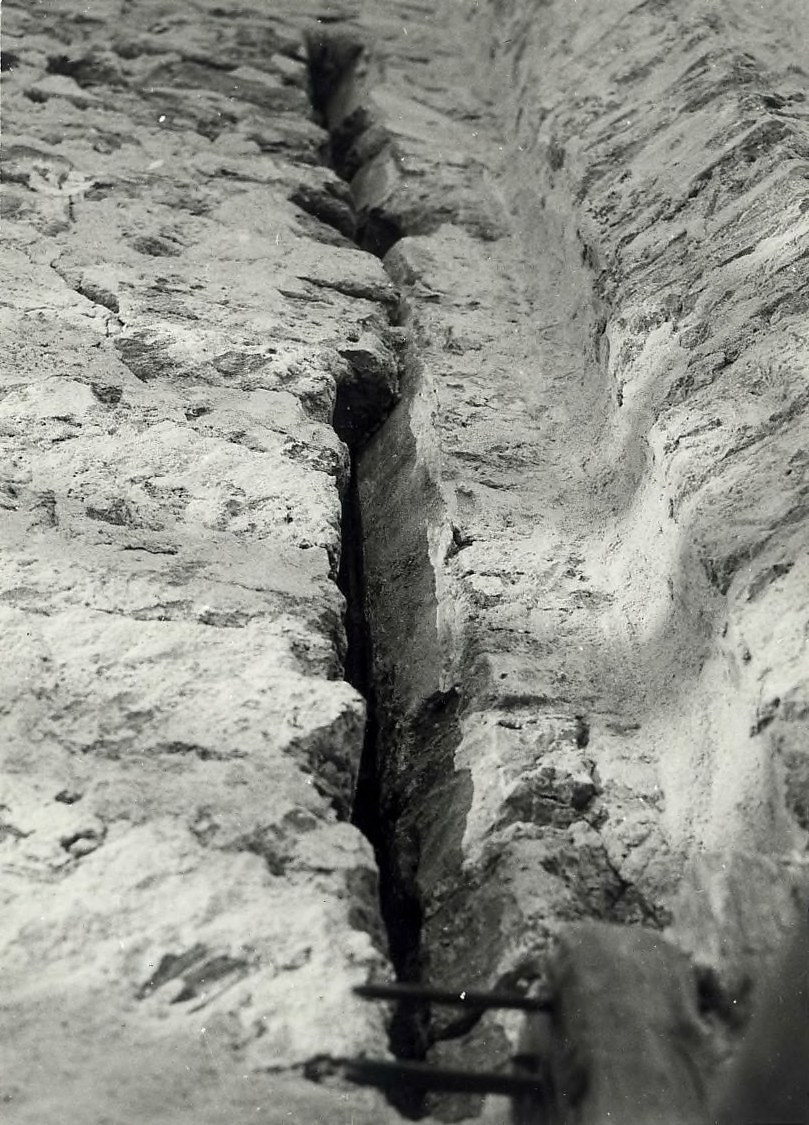 Schwarzes und weißes Foto eines großen Risses in einer Bodenentwässerung mit einem Wasserzeichen auf der linken Seite.