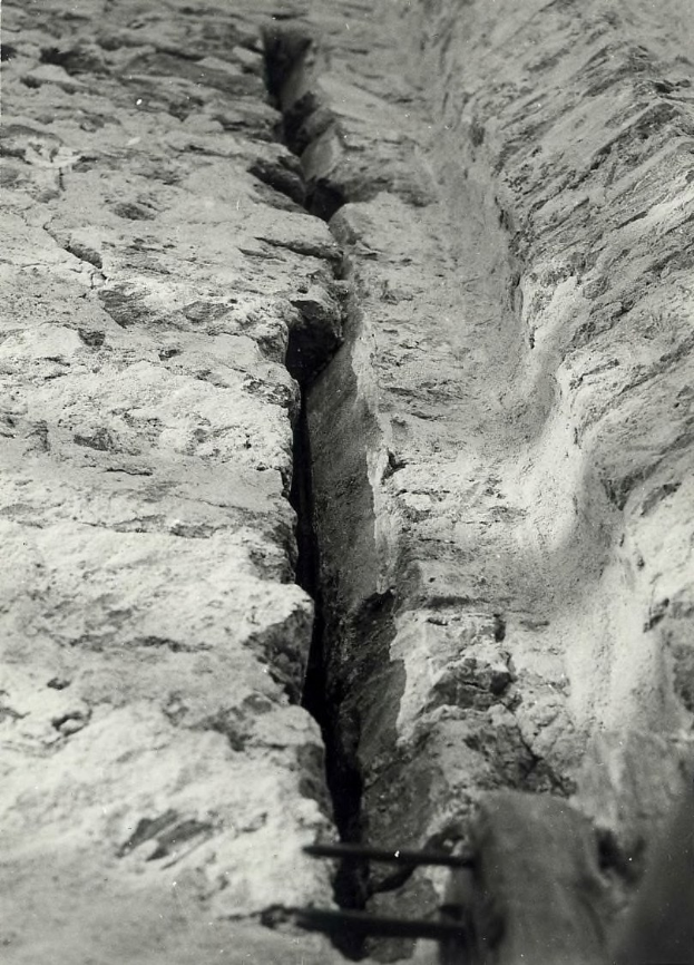 Schwarzes und weißes Foto eines großen Risses in einer Bodenentwässerung mit einem Wasserzeichen auf der linken Seite.