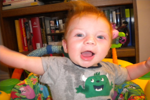 Ein Kind sitzt auf einem Stuhl vor einem teilweise sichtbaren Regal mit Bühchern, vor einem abgeschnittenen Wandhintergrund.