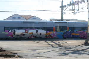 Graffiti-bedeckte Bahn mit sichtbaren Kabeln, Häuser mit Fenstern im Hintergrund.