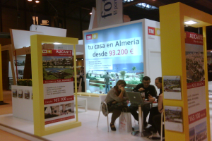 Eine Gruppe von Menschen sitzt an einem Tisch und schaut auf einen Laptop, neben ihnen liegen mehrere Flyer mit verschiedenen Werbeanzeigen.