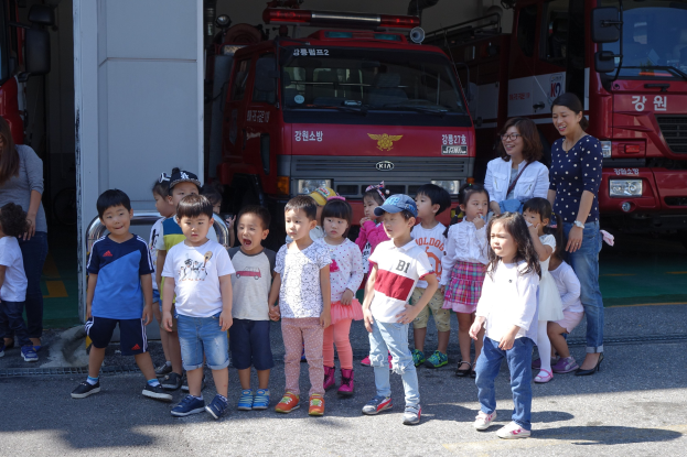 Gruppe von Kindern vor mehreren Feuerlöschwagen an einer Feuerwache, einige tragen Mützen.