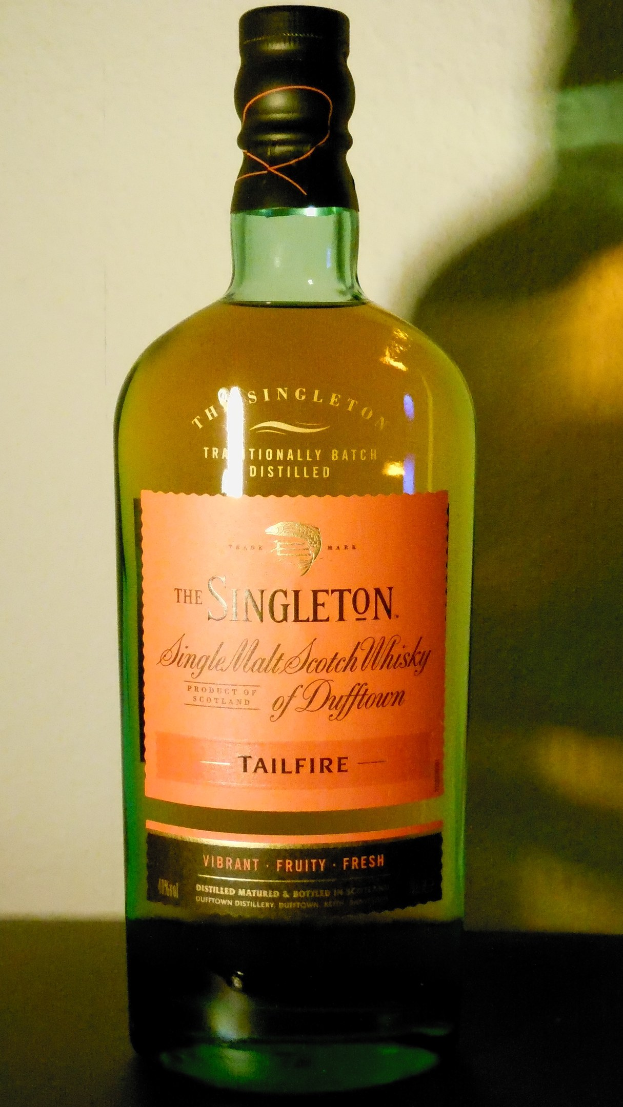 Eine tiefe bernsteinfarbene Flasche Singleton of Dufftown Tailfire Single Malt Scotch Whisky mit einem schwarzen Etikett, das eine schlagzeile und ein Wappen mit einem Löwen und einer Burg enthält.