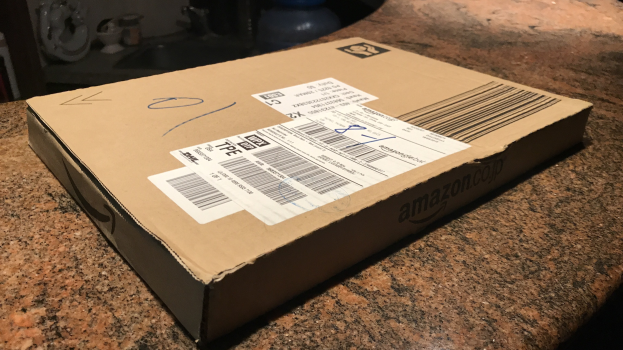 Kartonbox mit der Aufschrift 'Amazon Prime Day' auf einer Arbeitsplatte stehend mit ein paar Gegenständen im Hintergrund.