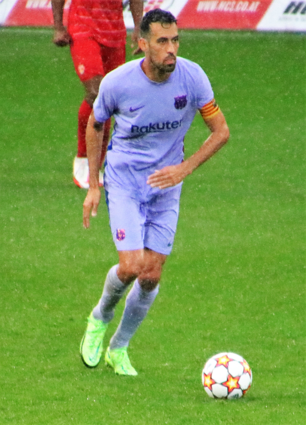 Ein Fußballspieler in einem Sportoutfit und Fußballschuhen ist im Einsatz auf dem Feld, mit einem Textschild im Hintergrund.