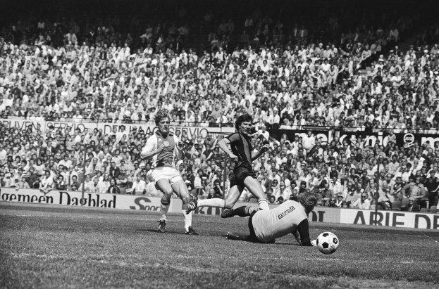 Schwarzes Foto von Männern, die auf einem Feld Fussball spielen, mit Zuschauern im Hintergrund und einem Banner mit der Aufschrift "Bundesliga 1978-79 Ajax 1-1 Hannover 96."