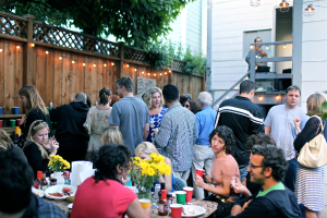Eine Gruppe von Menschen auf einer Party, einige sitzen um einen Tisch und andere stehen.