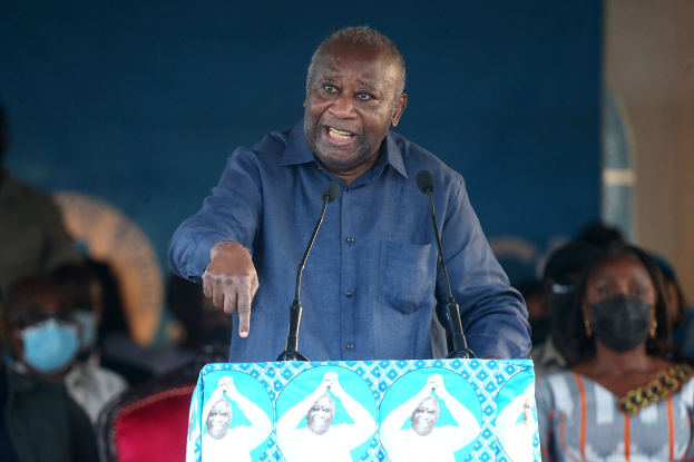 Ein Mann in einem blauen Hemd spricht an einem Pult mit zwei Mikrofonen, gewandt einem sitzenden öffentlichkeit, die Masken trägt, mit einer Wand im Hintergrund.