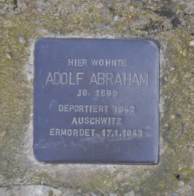 Rechteckige Plakette mit der Aufschrift "Adolf Abraham" an einer Steinwand angebracht.