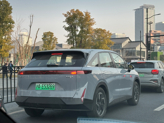 Ein Audi e-tron Elektroauto fährt auf einer städtischen Straße neben hohen Gebäuden, mit einem Geländer auf der linken Seite der Straße und Menschen, die auf dem Gehweg gehen, mit Bäumen, Gebäuden, Polen, Verkehrszeichen und einem klaren blauen Himmel im Hintergrund.