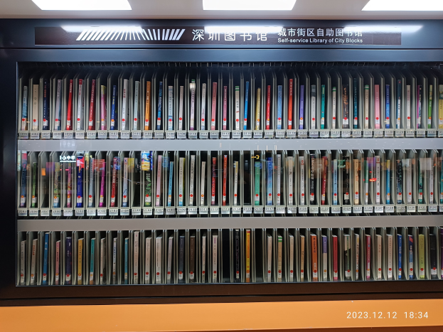 Eine gut beleuchtete Bibliothek mit Reihen von Bücherregalen, ein sichtbares Textbrett und ein Wasserzeichen unten, das an eine Selbstbedienungsbibliothek in Stadtblocks erinnert.