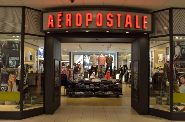 Aeropostale-Laden im Einkaufszentrum mit Schaufensterpuppen in Kleidern, Kleiderständern, Infotafeln, Glaswänden und Beleuchtung sowie einem Schild mit der Aufschrift 'Schließung im Juni'.