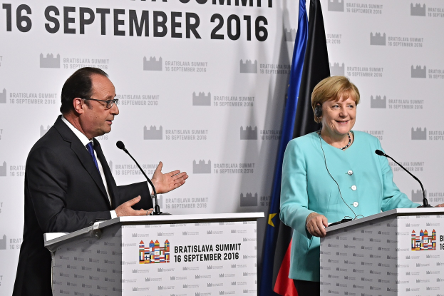 Bundeskanzlerin Angela Merkel und Frankreichs Präsident François Hollande stehen vor zwei Podien mit Mikrofonen, beide lächeln, mit einem Banner im Hintergrund, auf dem "Bratislava-Gipfel 2016" steht.