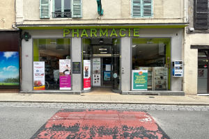 Eine Apotheke mit Glaswänden und -türen an einer Straßenecke, mit Plakaten an den Wänden und einer Straße unten.