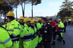 Gruppe von Einsatzkräften in gelben Westen und Helmen auf einer Straße mit Bäumen und einem klaren blauen Himmel.
