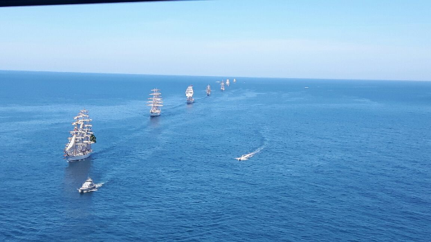 Eine große Gruppe von Segelschiffen nimmt an einem Regatta teil, die auf einem klaren blauen Meer unter der strahlenden Sonne segelt.