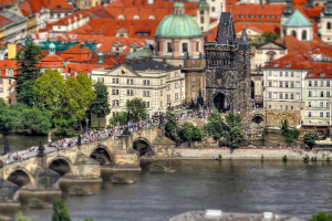 Eine Stadtansicht mit zahlreichen Gebäuden, einem Turm, Bäumen, Menschen und einer Brücke, die den Fluss überquert.