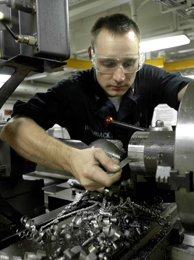 Ein Monteur mit Brille bedient eine Maschine in einer hell erleuchteten Fabrik.
